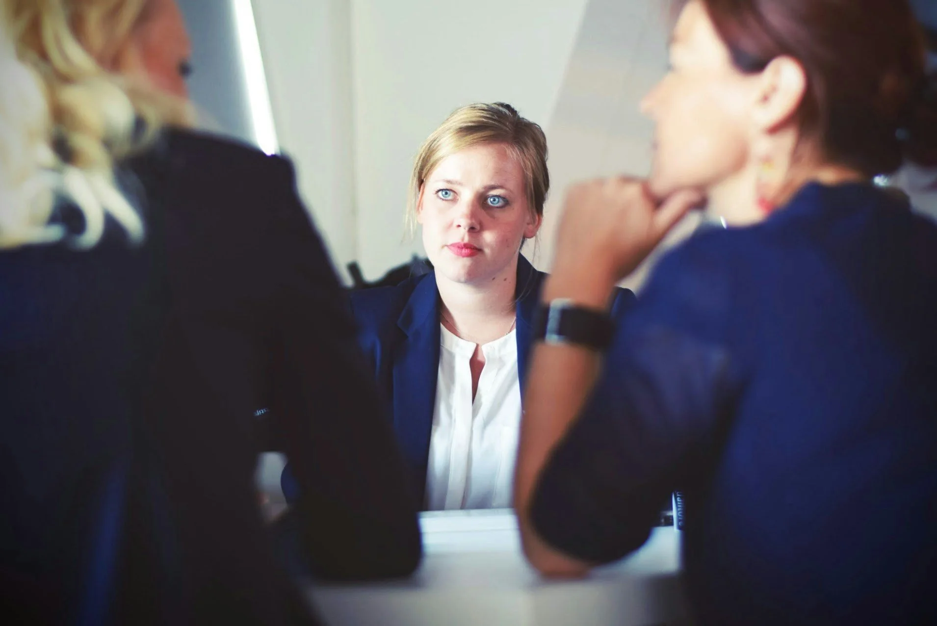 Three women in business attire at a table during a meeting or interview.