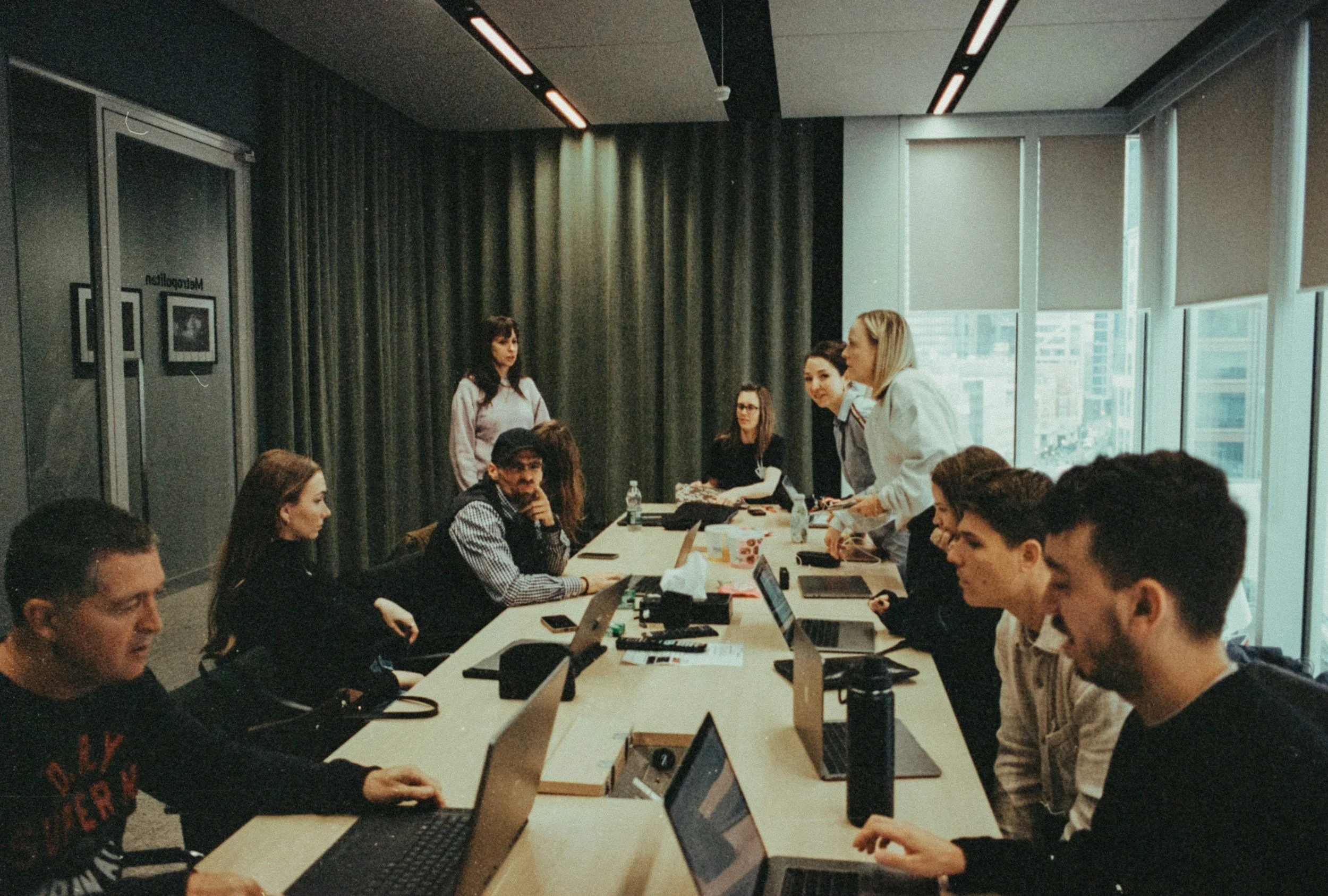 Diverse group of people in a modern office meeting room, working on laptops.