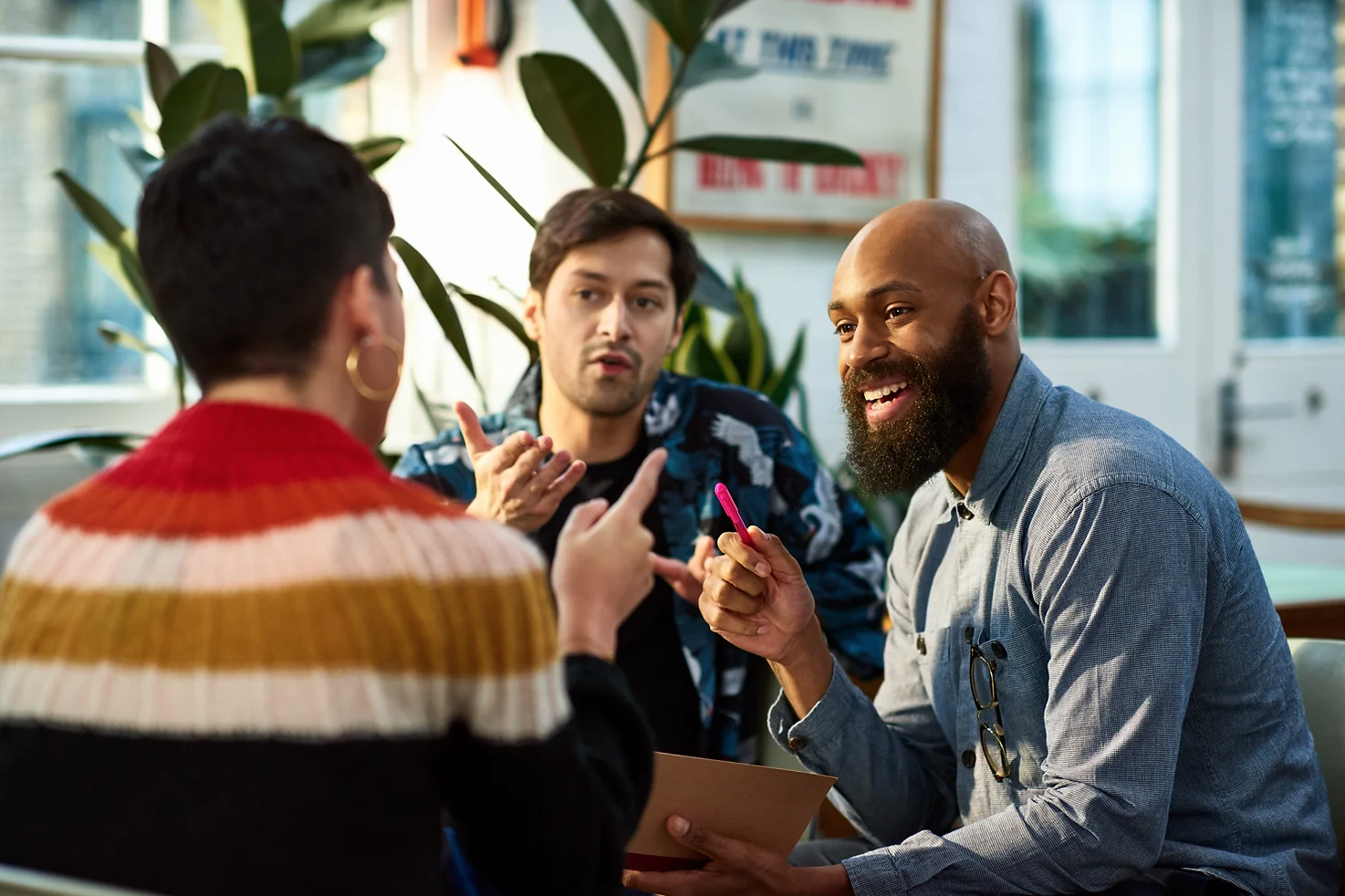 Three people in a discussion. Two men and one person with short dark hair wearing a colorful sweater.