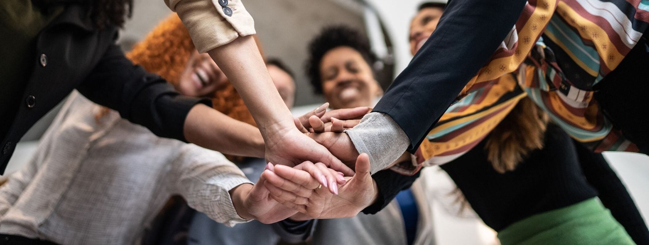 Diverse group of people in a huddle, hands clasped together in unity and support.
