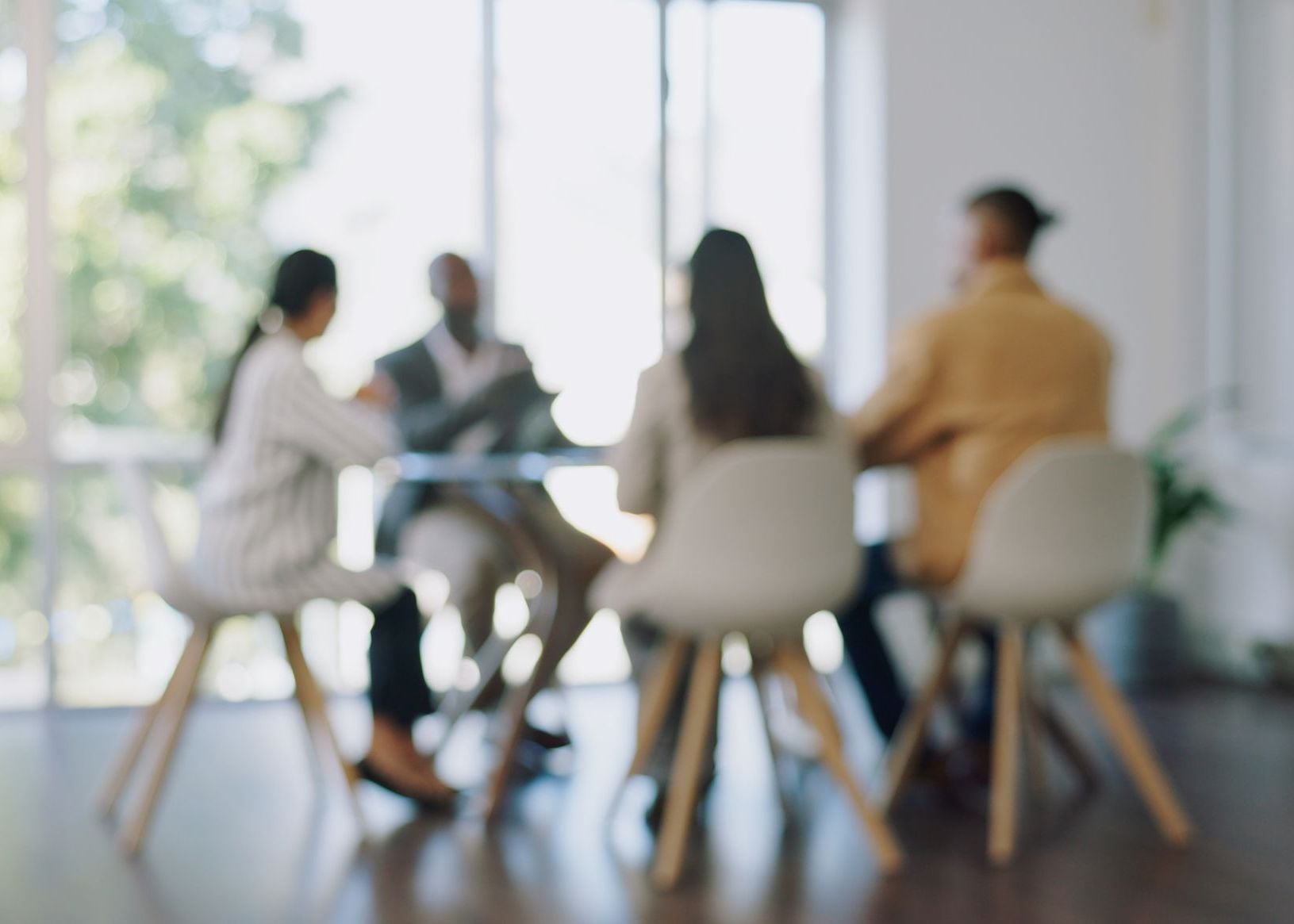 Blurred image of four diverse colleagues in a meeting room, discussing ideas at a table.